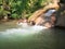 Little boy cheerfully laughs and shows a positive sign with his hand on a background of small bubbling waterfall