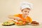 Little boy in chef hat puts meat on hamburger