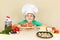 Little boy in chefs hat appetizing licked near cooked pizza