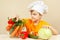 Little boy in chefs hat chooses vegetables for salad at table