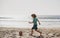 Little boy child play football on coast of sea beach. Summer kids sports.