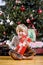 Little boy by Christmas tree holding present