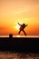 A little boy in a coat with a suitcase, jumping with happiness on the pier at sunset.