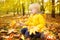 Little boy collecting maple leaves during stroll in the forest at sunny autumn day. Active family time on nature