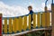 The little boy concentrates walking along the curved bridge of the playground. Curved yellow fence, light blue sky with white