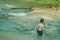 Little boy crossing a river full of stones carefully and teetering in waterfall at Erawan National Park