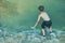 Little boy crossing a river full of stones carefully and teetering in waterfall at Erawan National Park