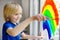 Little boy drawing on window rainbow while coronavirus quarantine. Rainbow sign is symbol of hope, means that everything will be