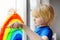 Little boy drawing on window rainbow while coronavirus quarantine. Rainbow sign is symbol of hope, means that everything will be