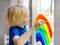 Little boy drawing on window rainbow while coronavirus quarantine. Rainbow sign is symbol of hope, means that everything will be