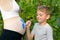 Little boy draws with a brush on the belly of his pregnant mom babyâ€™s footprint. Pregnant concept. Close-up