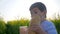 Little boy drinking from glass with loaf bread in hand outdoors, child drink clean water on meadow in backlight