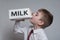 Little boy drinks from a large white milk package. White shirt and red tie. Light background