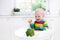 Little boy eating broccoli in white kitchen