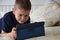 little boy at expressive face using a digital tablet in bed plays games, watch cartoons, talks with friends, writes a