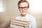 Little boy in eyeglasses holding pile of books and smiling at camera