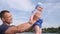 Little boy in father`s strong hands in blue sky background, beautiful male raises son up in arms on lake,