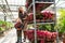 Little boy with a flower in a pot and his mom, a florist who pulls a cart with flowers in a greenhouse.