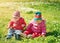 Little boy and girl in hats sitting on the field with soft toys in summer