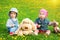 Little boy and girl in hats sitting on the field with soft toys in summer