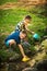 Little boy and girl play draw water in bucket from stream