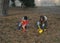 A little boy and girl in rubber boots are walking through the forest and holding shovels.