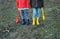 A little boy and girl in rubber boots are walking through the forest and holding shovels.