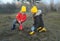 A little boy and girl in rubber boots are walking through the forest and holding shovels.