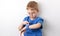 A little boy with glasses and a blue T-shirt looks at his smart watch against the background of a white wall.