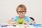 Little boy in glasses sitting at desk with school supplies, doing homework at table. Back to school. Preschool boy playing in busi