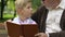 Little boy and grandfather reading book, relaxing on bench in park, education