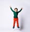 Little boy in green jumper, orange pants, blue sneakers. He jumping with raised hands, smiling, posing isolated on white