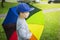 Little boy in hat with multicolor umbrella in park after rain on sunny summer day