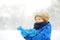 Little boy having fun playing with fresh snow during snowfall. Admiring baby catching snowflakes on gloves. Active outdoors