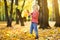 Little boy having fun during stroll in the forest at sunny autumn day. Child collect maple leaves. Inquisitive baby explore nature