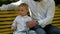 Little boy and his dad does not want to try on a bow tie. They are sitting on a park bench. Father`s day.