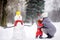 Little boy with his mother/babysitter/grandmother building snowman in snowy park