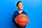 Little boy hispanic kid holding basketball ball smiling looking to the side and staring away thinking