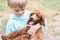 little boy is holding a brown poodle puppy in his arms