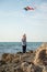 Little boy holding a kite standing on a rock against the sea