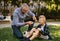 Little boy with injured leg crying, his grandfather is giving him plaster outdoors in park.