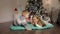 A little boy kisses a girl near a Christmas tree.