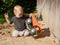 Little boy kneels on the sand in the courtyard of the house and plays with a huge toy dump truck.