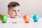 The little boy laid his head on a white table on which multi-colored Easter eggs stand in a row on a white background