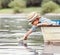 Little boy launch paper ship from old boat on the lake