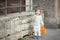 Little boy with long blond hair crying standing on the street. In his hand he is holding an orange bucket to play in the sandbox