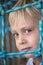 Little boy looks thoughtfully at the camera. Child looks through the mesh. Portrait vertical frame