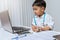 Little boy in medic uniform holding a pen and look at laptop on desk