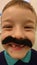 Little boy with no front teeth wearing a fake moustache