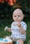 A little boy one 1 year old sits on the green grass in the garden and eats a sweet birthday cake, a funny smeared kid close-up